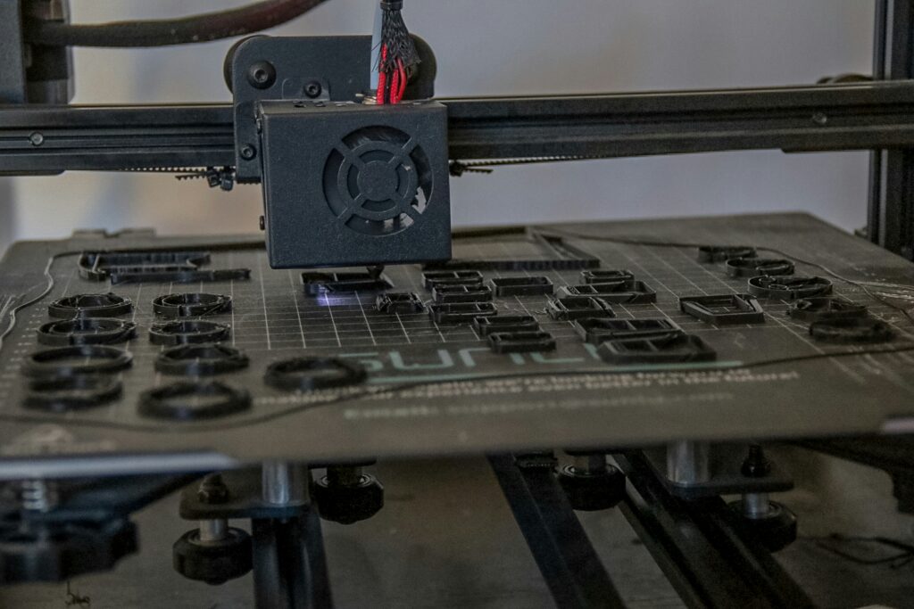 3d printer maintenance showing a nozzle being cleaned with a needle and a print bed with adhesive representing common 3d printer fixes and upkeep