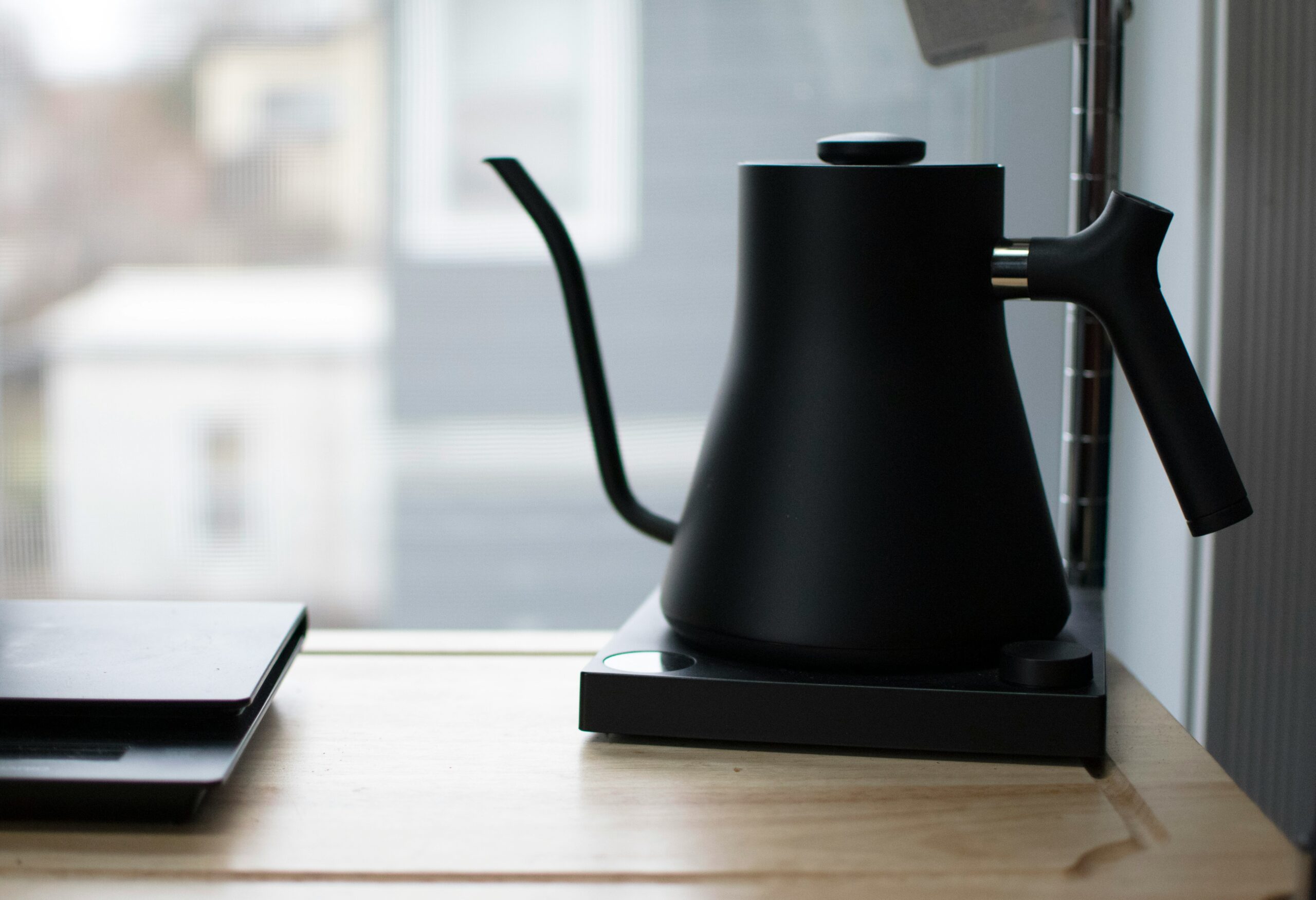 best gooseneck kettle showing Fellow Stagg EKG electric gooseneck kettle and Hario Buono stovetop kettle on a kitchen counter next to pour over coffee brewing setup